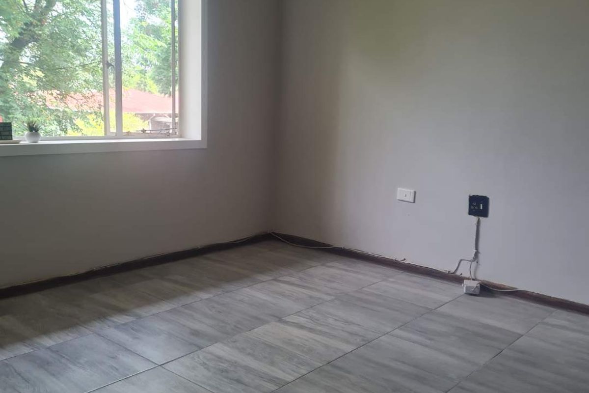 An empty bedroom featuring grey tiled flooring and a window with natural light, ready for personalization.