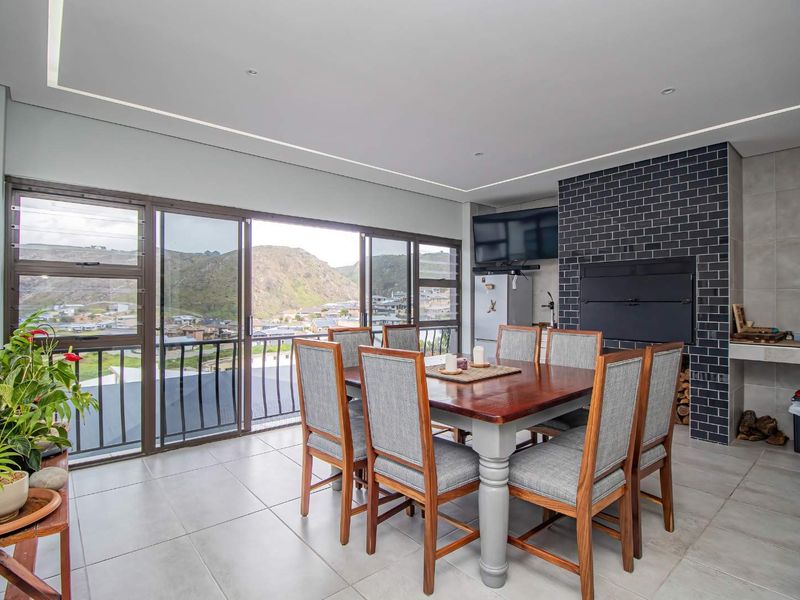 Covered patio area featuring a built-in braai, dark brick feature wall, large sliding glass doors, and scenic mountain views.