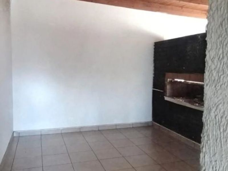 A covered patio area featuring a rustic timber ceiling, tiled flooring, and a built-in braai, offering a versatile space for outdoor entertaining.