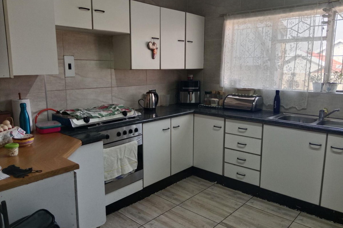 A functional kitchen featuring white cabinetry, laminate countertops, tiled flooring, and a stainless steel sink with a window view.