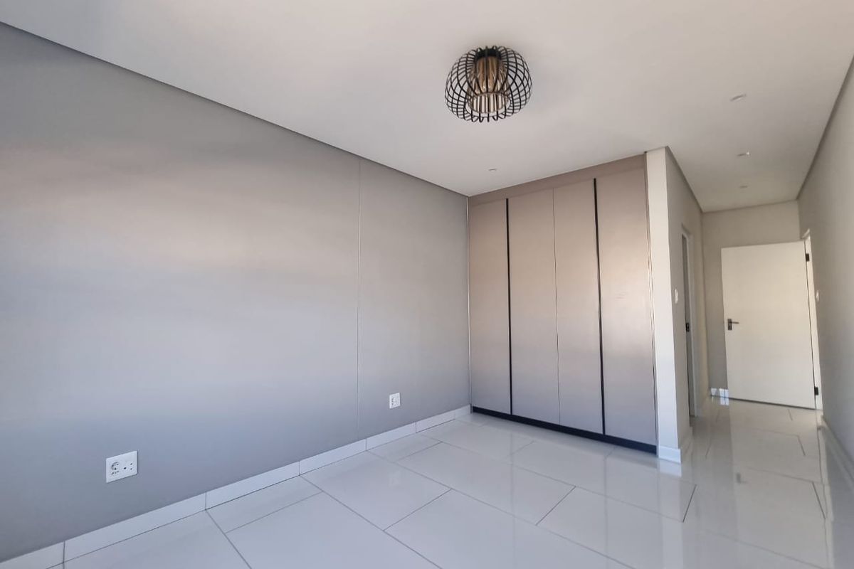 A bright, modern bedroom featuring sleek tiled flooring, neutral grey walls, and ample built-in cupboard storage.