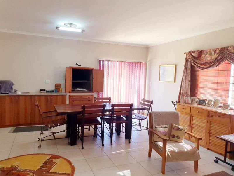 Open plan living and dining area featuring tiled floors, built-in indoor braai, and large windows with blinds, offering a functional and versatile space.