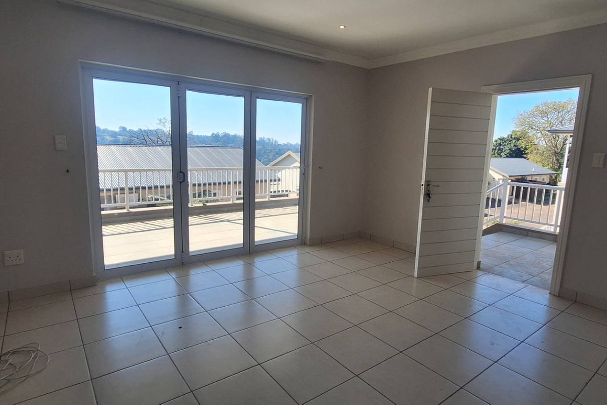 A bright, empty bedroom featuring tiled flooring, recessed lighting, and direct access to a private balcony through sliding glass doors.