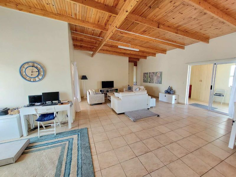 Spacious open-plan living area featuring high exposed timber beam ceilings and neutral tiled flooring, with sliding door access to an adjoining space.