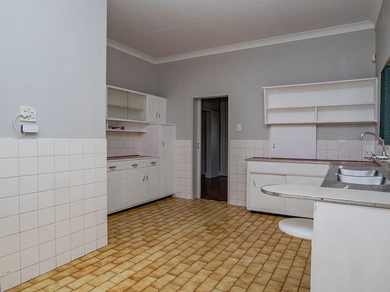 A dated, empty kitchen featuring original built-in cabinetry, a double basin sink, and tiled flooring, offering significant potential for a modern renovation.