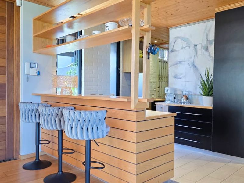 Modern kitchen featuring a timber breakfast bar with integrated shelving, black cabinetry, and warm timber ceiling finishes.