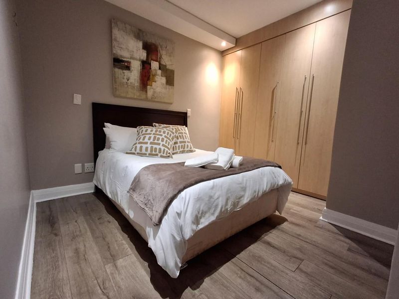 A well-maintained bedroom featuring modern laminate flooring, recessed ceiling lighting, and extensive built-in wooden cabinetry for storage.