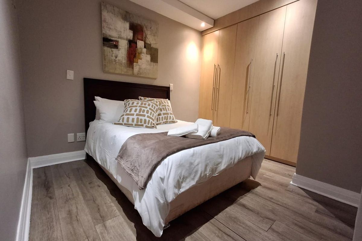 A well-maintained bedroom featuring modern laminate flooring, recessed ceiling lighting, and extensive built-in wooden cabinetry for storage.