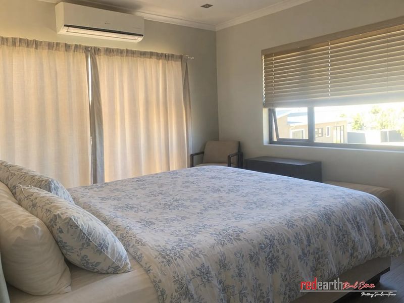 A well-lit bedroom featuring a split-system air conditioner, neutral wall finishes, and large windows with fitted blinds.