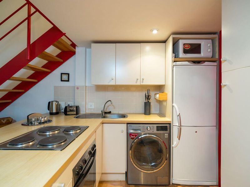 Compact kitchen featuring built-in cabinetry, electric hob, oven, and integrated washing machine, conveniently located beneath a staircase.