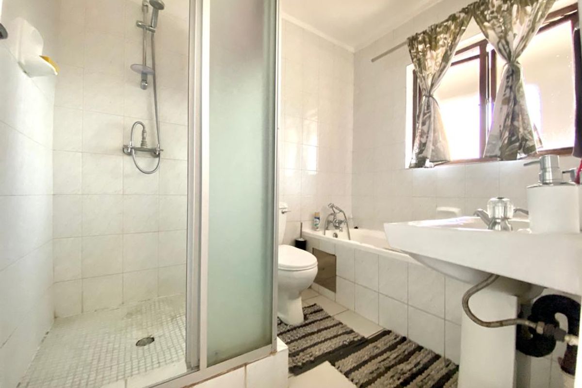 A functional bathroom featuring a glass-enclosed shower, a standard bathtub, and a pedestal sink with tiled walls and flooring.