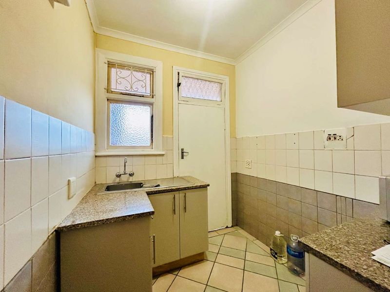 A compact, dated kitchen featuring tiled splashbacks, granite countertops, and base cabinetry, offering a functional layout ready for modernization.