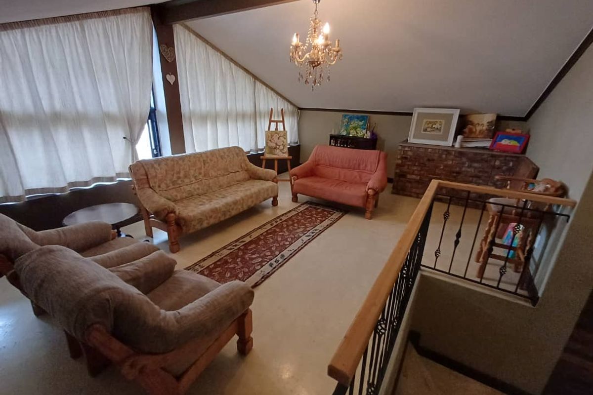 Spacious living area featuring a vaulted ceiling, exposed timber beams, and a brick feature wall, overlooking the lower level via a wrought iron balustrade.