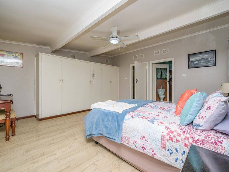 Spacious bedroom featuring built-in cupboards, exposed ceiling beams, and a ceiling fan, with direct access to an en-suite bathroom.