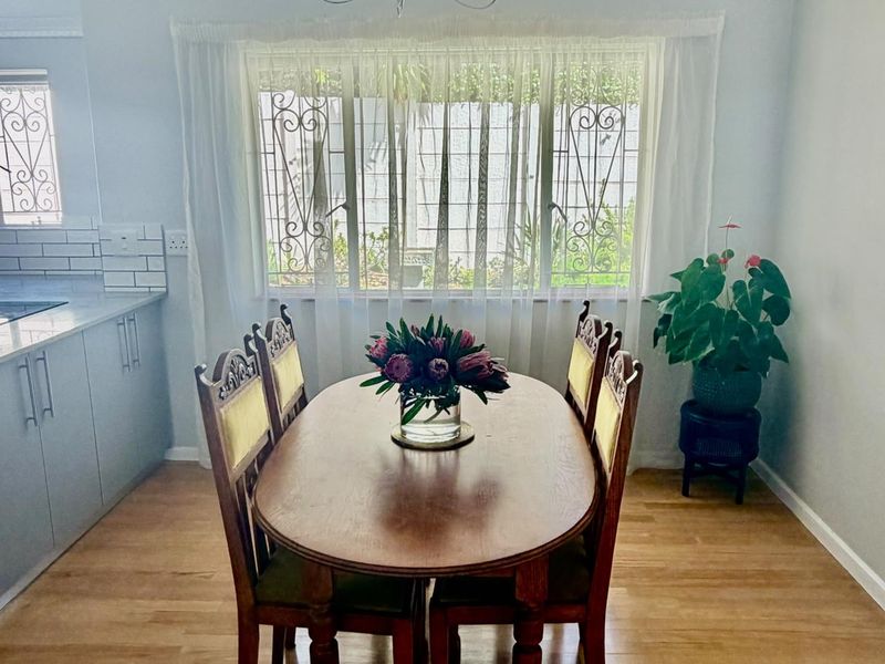A bright dining area featuring laminate flooring, adjacent kitchen cabinetry with subway tile backsplash, and large windows fitted with security bars.