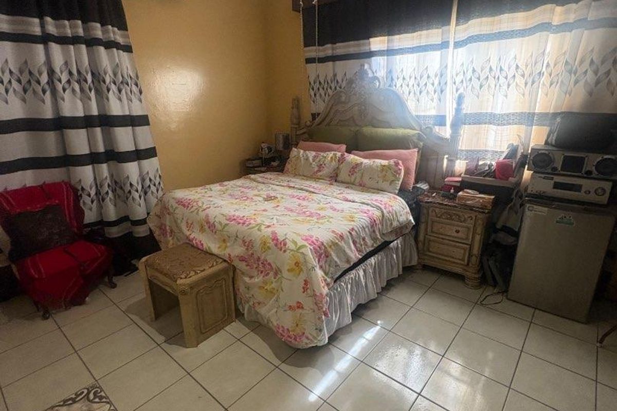 A bedroom featuring tiled flooring, a wall-mounted air conditioning unit, and a ceiling fan, showing signs of ceiling water damage.