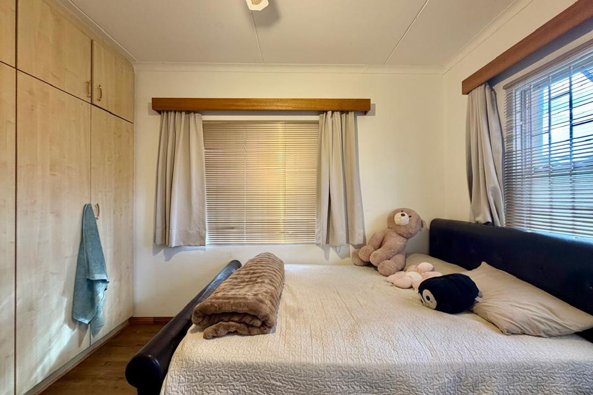 A bedroom featuring built-in wooden cabinetry, wooden flooring, and windows fitted with blinds and wooden pelmets.