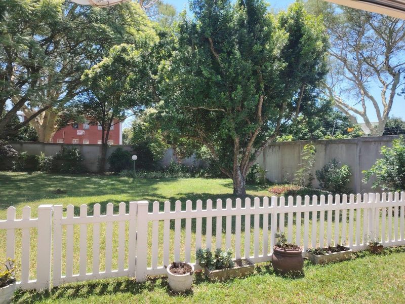 A well-maintained private garden featuring a white picket fence, established trees, and a concrete boundary wall providing privacy.