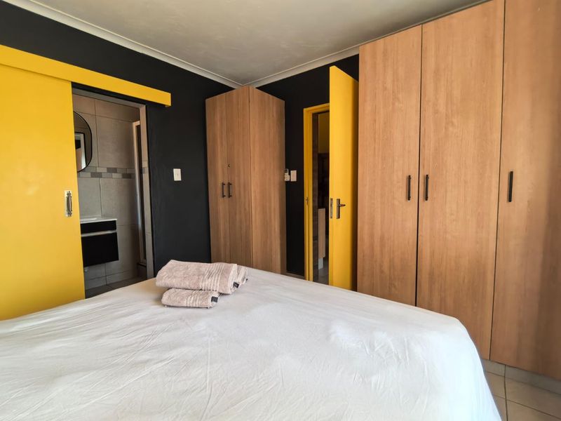 Bedroom featuring built-in wooden cupboards, dark accent walls, yellow door frames, and direct access to an en-suite bathroom.
