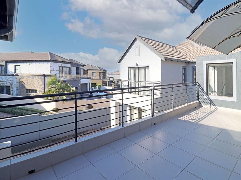 A spacious, tiled balcony featuring a secure metal balustrade and overhead cover, offering views of the surrounding residential estate.