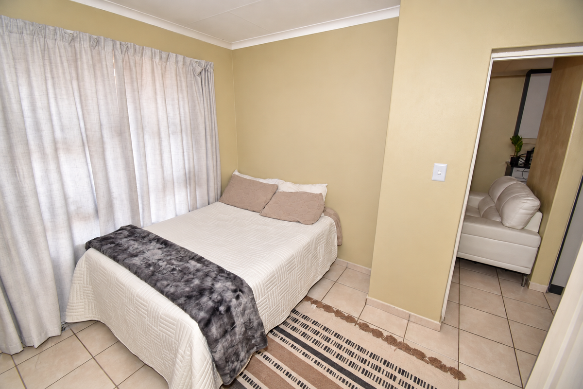 A functional bedroom featuring neutral wall tones, tiled flooring, and a coved ceiling, with direct access to an adjacent living space.