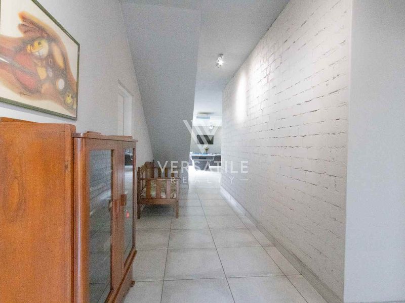 A long interior hallway featuring tiled flooring and a textured exposed brick wall, leading towards the main living area.
