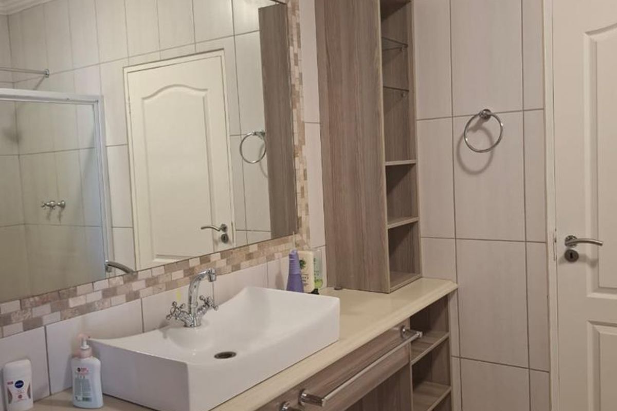 A well-maintained bathroom featuring a modern vessel sink, built-in vanity cabinetry with open shelving, a large framed mirror, and neutral wall tiling.