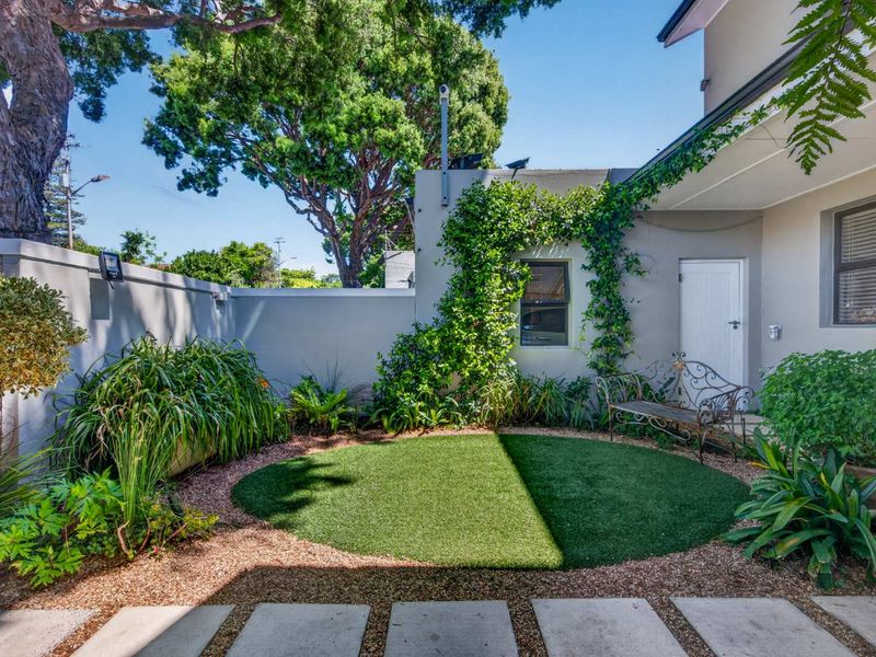 A well-maintained rear courtyard featuring artificial turf, gravel landscaping, concrete pavers, and established climbing plants against a secure boundary wall.