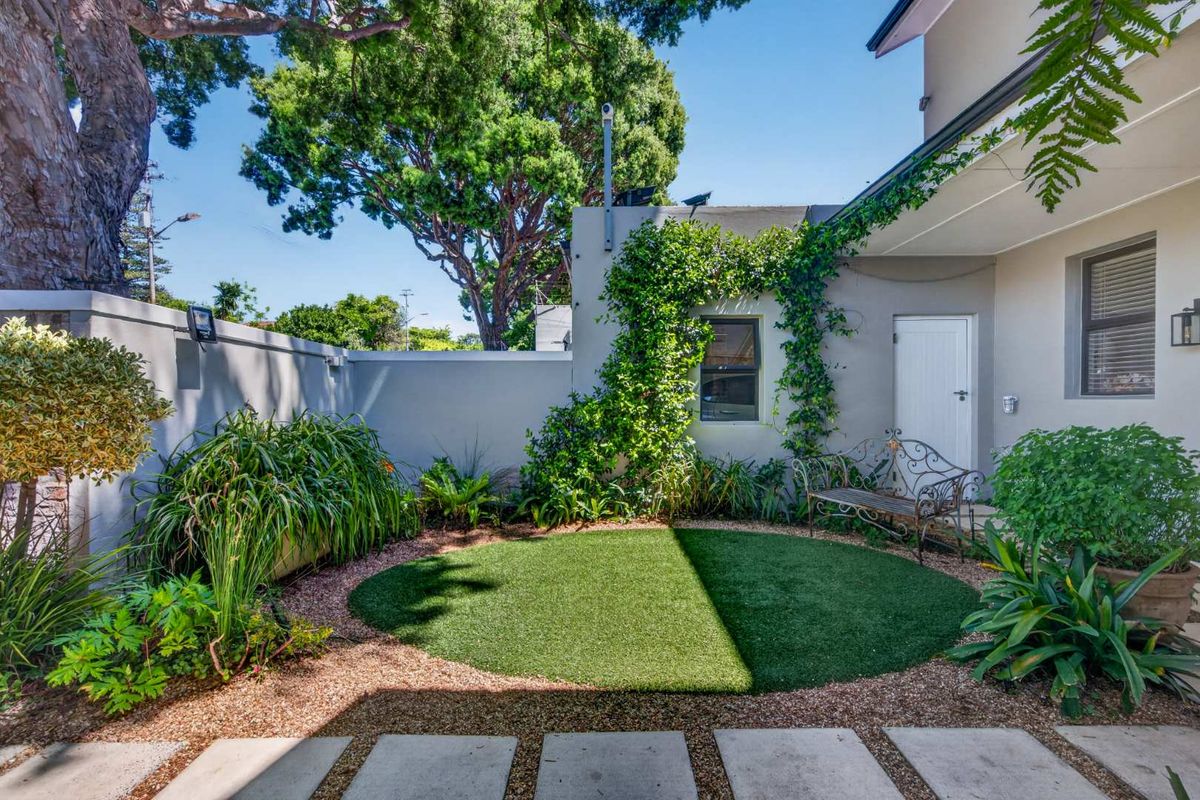 A well-maintained rear courtyard featuring artificial turf, gravel landscaping, concrete pavers, and established climbing plants against a secure boundary wall.