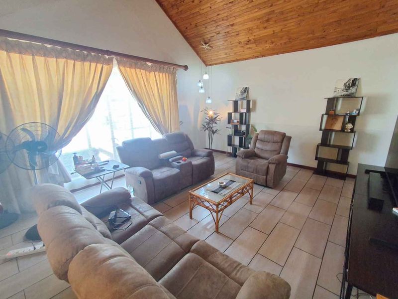 Spacious living room featuring a high vaulted timber ceiling, tiled flooring, and large sliding glass doors that provide ample natural light.
