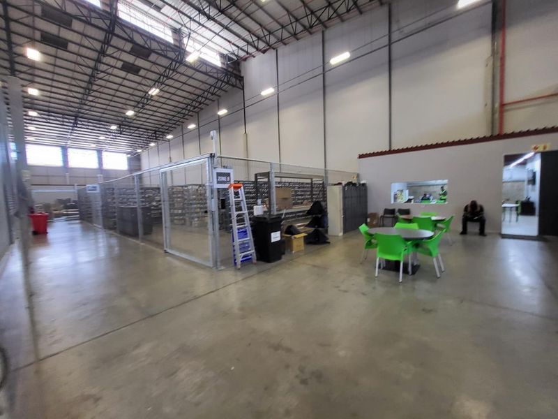 Spacious industrial warehouse featuring high-volume ceilings, concrete flooring, and a partitioned secure storage zone with wire mesh fencing.