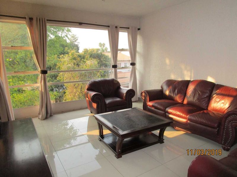 A bright living room featuring large windows with natural light, tiled flooring, and textured wall finishes, offering a comfortable and airy living space.