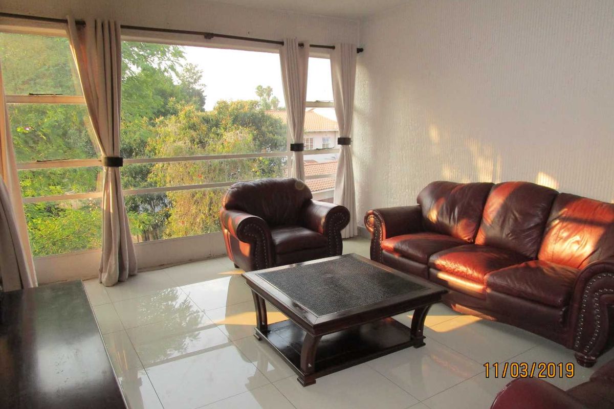 A bright living room featuring large windows with natural light, tiled flooring, and textured wall finishes, offering a comfortable and airy living space.