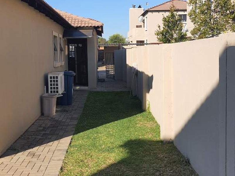 A side garden area featuring a paved walkway, boundary wall, and an exterior air conditioning unit.