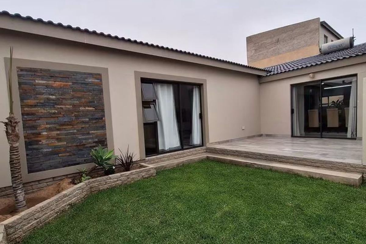 A well-maintained rear exterior featuring a landscaped lawn, stone-clad feature wall, tiled patio area, and modern sliding glass doors providing indoor-outdoor flow.