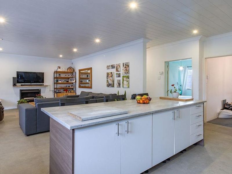 An open-plan living and kitchen area featuring a central island, built-in fireplace, recessed lighting, and neutral tiled flooring throughout.