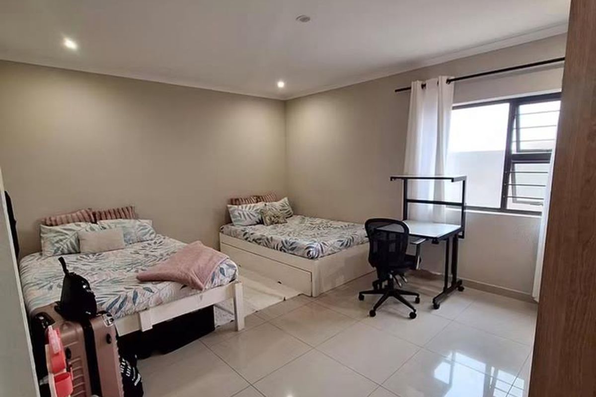 Spacious bedroom featuring large format floor tiles, recessed downlighting, and an aluminium-framed window, offering a clean and neutral living space.