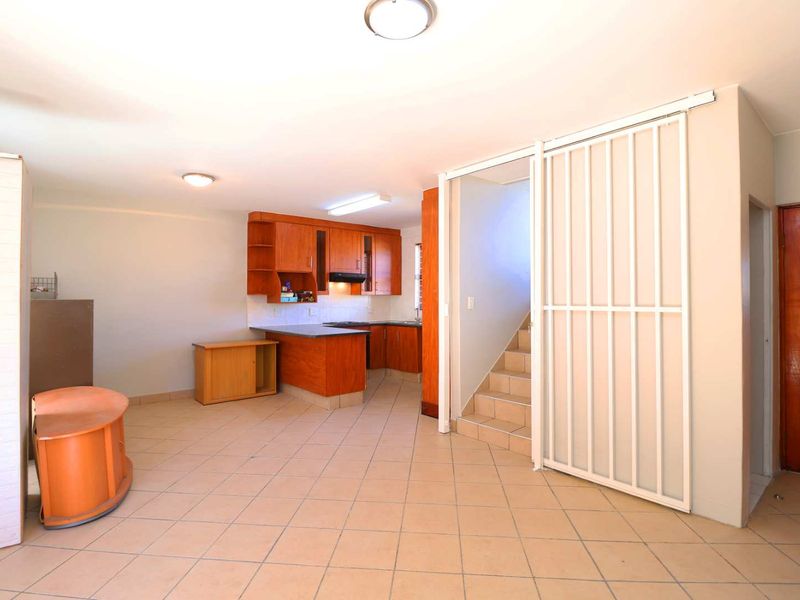 Open plan living area featuring tiled floors, a functional wooden kitchen with built-in cabinetry, and a staircase with a security gate.