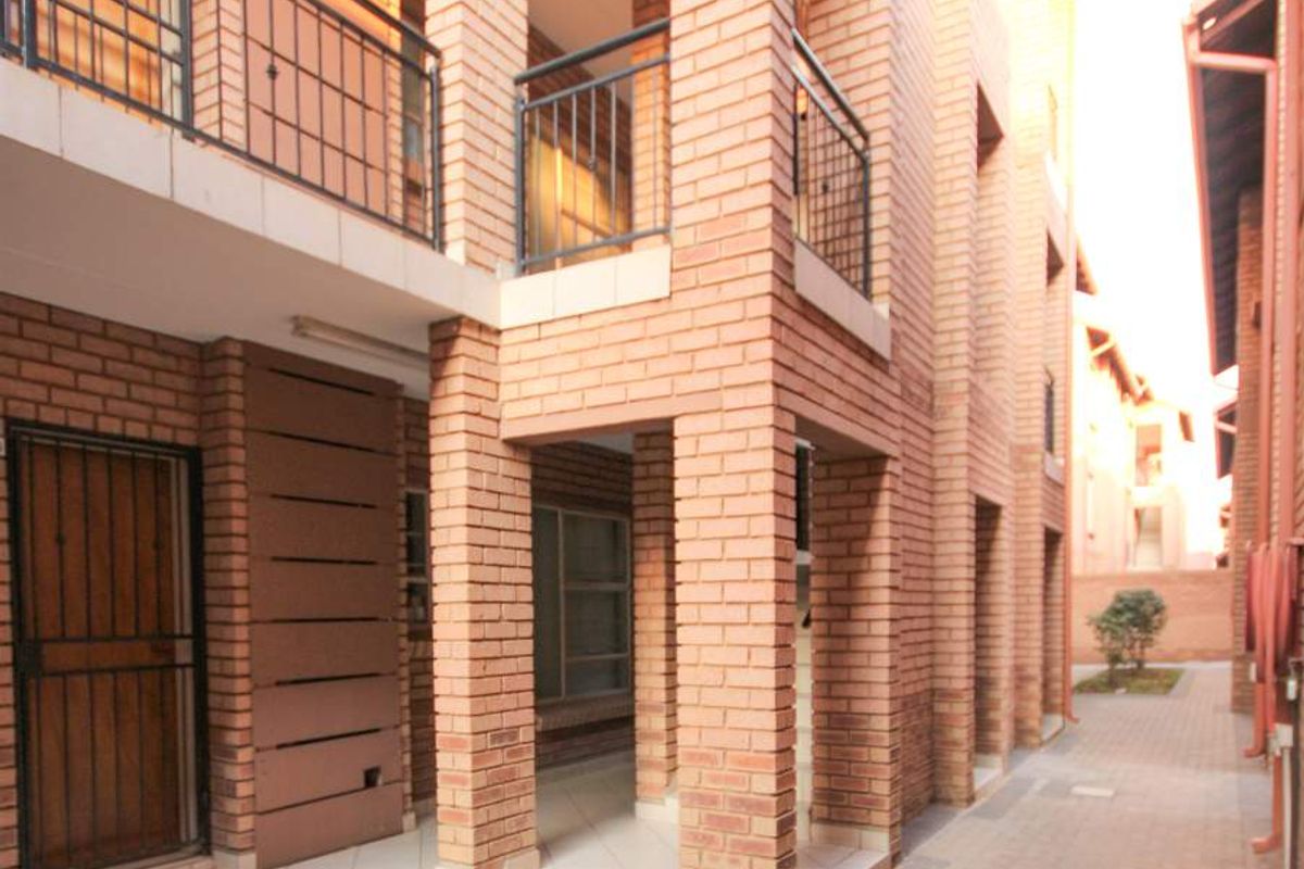 Exterior view of a multi-story apartment complex featuring exposed brick facade, paved walkways, and metal balcony railings.
