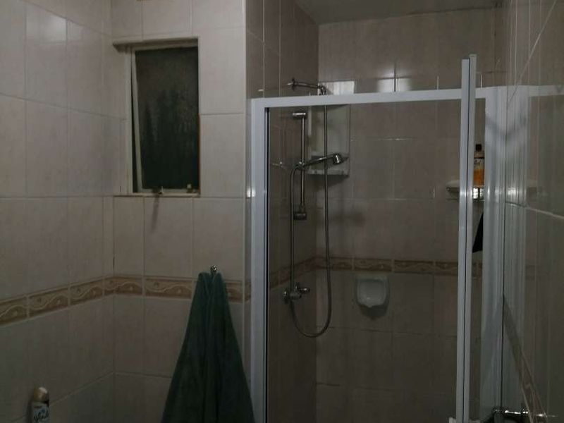 A compact bathroom featuring a shower enclosure, toilet, and tiled walls. The space is dated and would benefit from modern finishes and improved lighting.