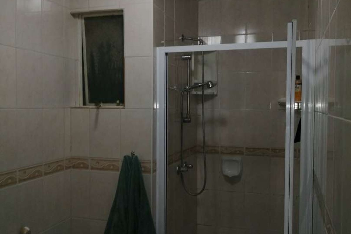 A compact bathroom featuring a shower enclosure, toilet, and tiled walls. The space is dated and would benefit from modern finishes and improved lighting.