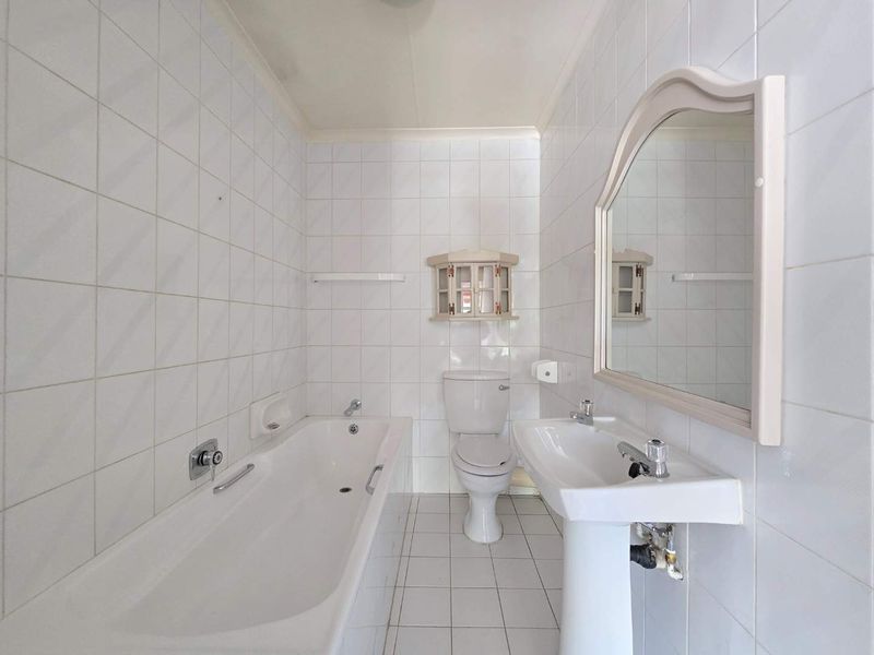 A functional bathroom featuring a white bathtub, pedestal basin, and toilet, finished with classic white wall and floor tiling.