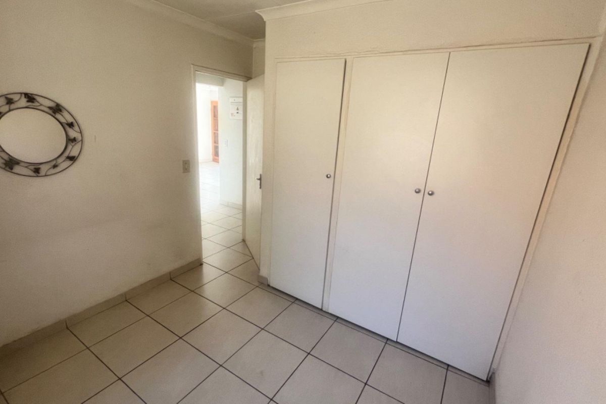 A bedroom featuring built-in cupboards with white doors and tiled flooring, leading into an adjacent room.