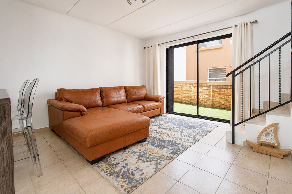 A bright living room featuring tiled flooring, a staircase with a black metal railing, and large sliding glass doors opening to a rear patio area.