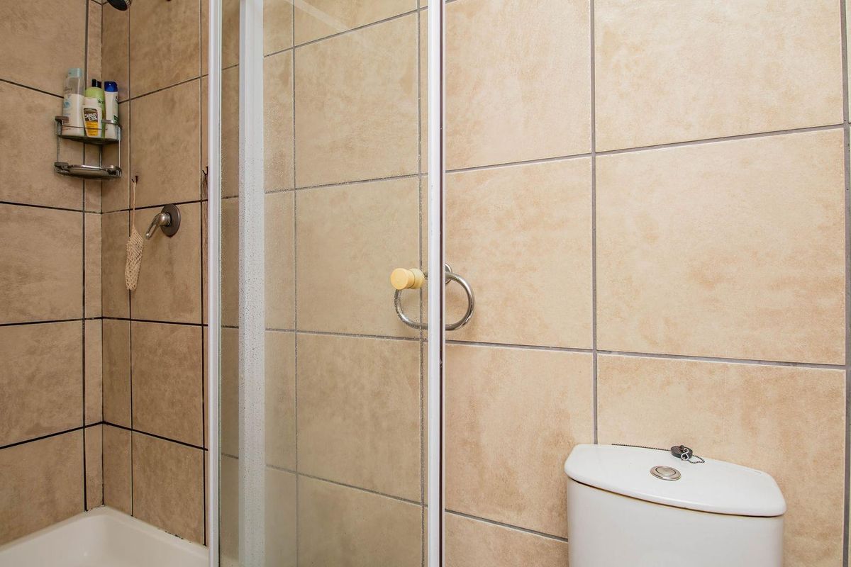 A functional bathroom featuring a shower enclosure with beige wall tiles and a standard white toilet.