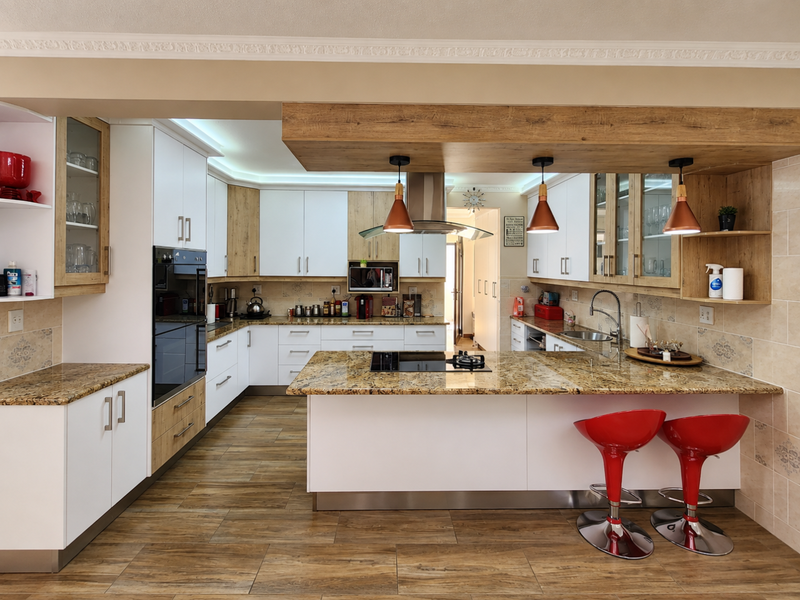 Modern kitchen featuring granite countertops, built-in oven, electric hob, extractor fan, and ample cabinetry with a central island and breakfast bar seating.