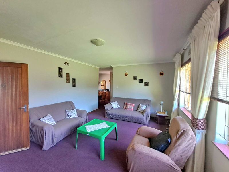 A spacious living room featuring neutral wall finishes, coving, and large windows with fitted blinds, offering a comfortable and functional living space.