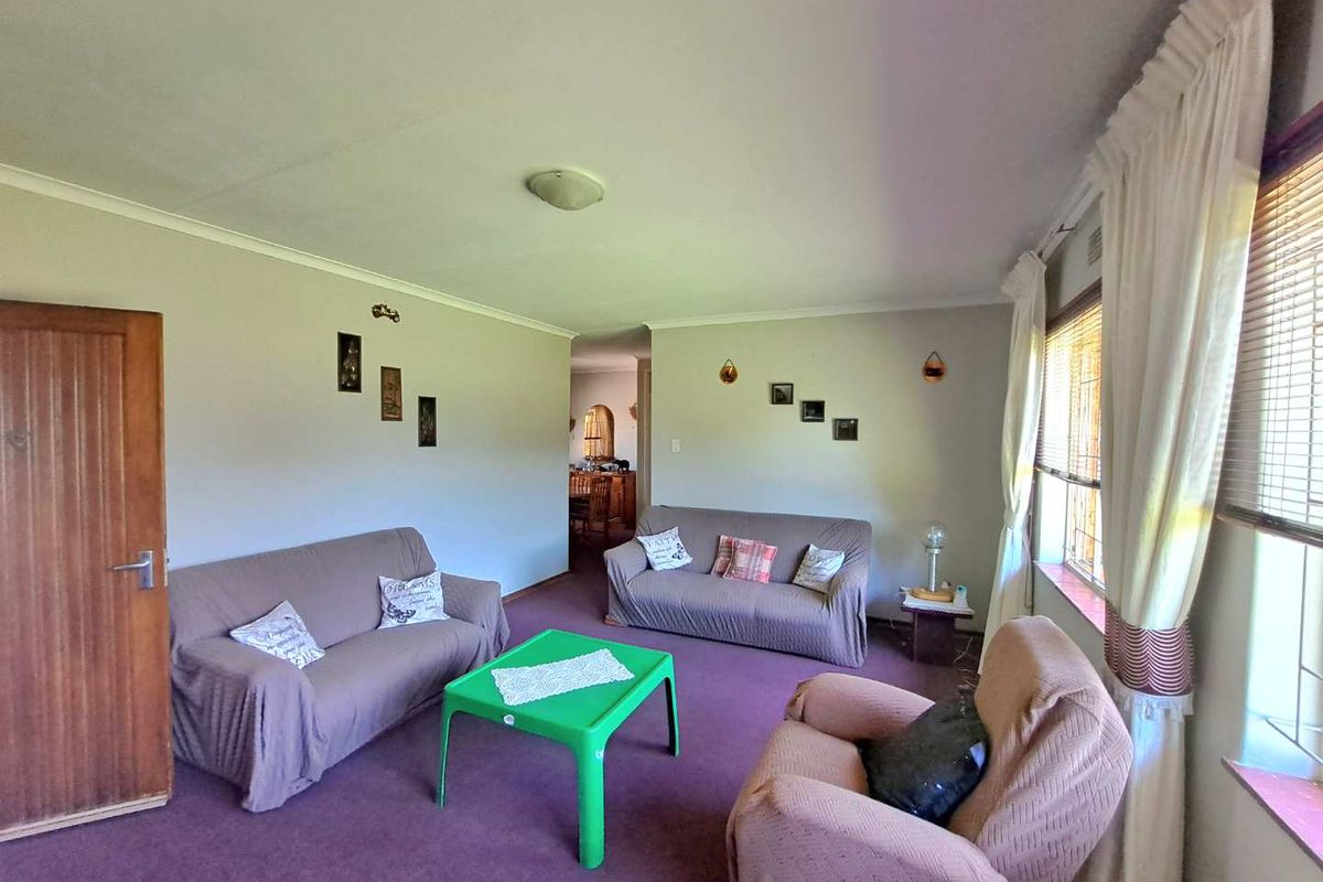 A spacious living room featuring neutral wall finishes, coving, and large windows with fitted blinds, offering a comfortable and functional living space.