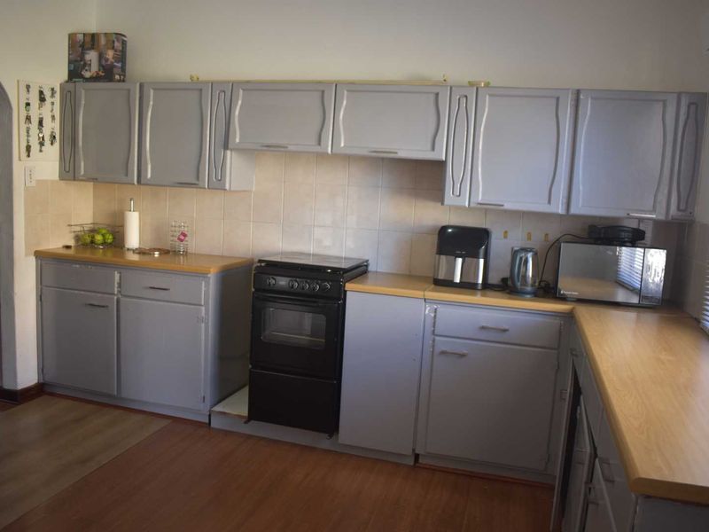 A functional kitchen featuring grey painted cabinetry, light wood-look laminate countertops, a tiled backsplash, and a freestanding oven.