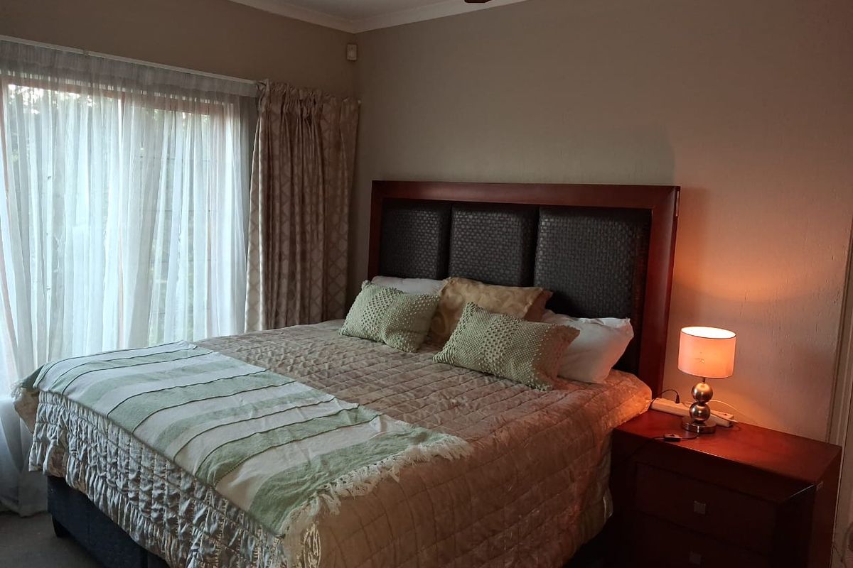 A comfortable bedroom featuring a built-in headboard, ceiling fan, and large sliding glass doors with curtains providing natural light.